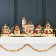 Pre-lit wooden Christmas village with warm LED lights arranged as festive mantel decor