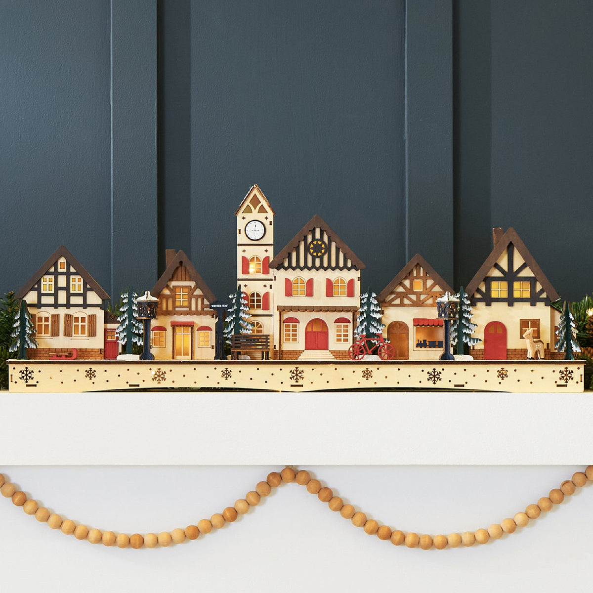 Pre-lit wooden Christmas village with warm LED lights arranged as festive mantel decor