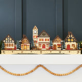 Pre-lit wooden Christmas village with warm LED lights arranged as festive mantel decor